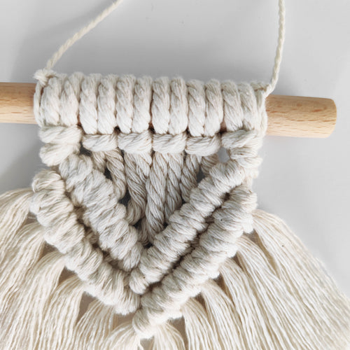 Macrame wall hanging with wooden rod on a light gray background